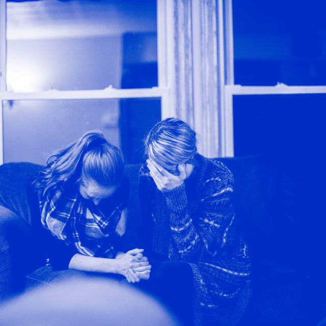Two women cry and sit close together on a couch