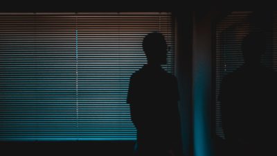 A person stands in the dark looking out a window