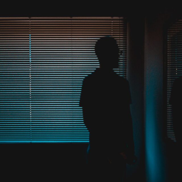 A person stands in the dark looking out a window