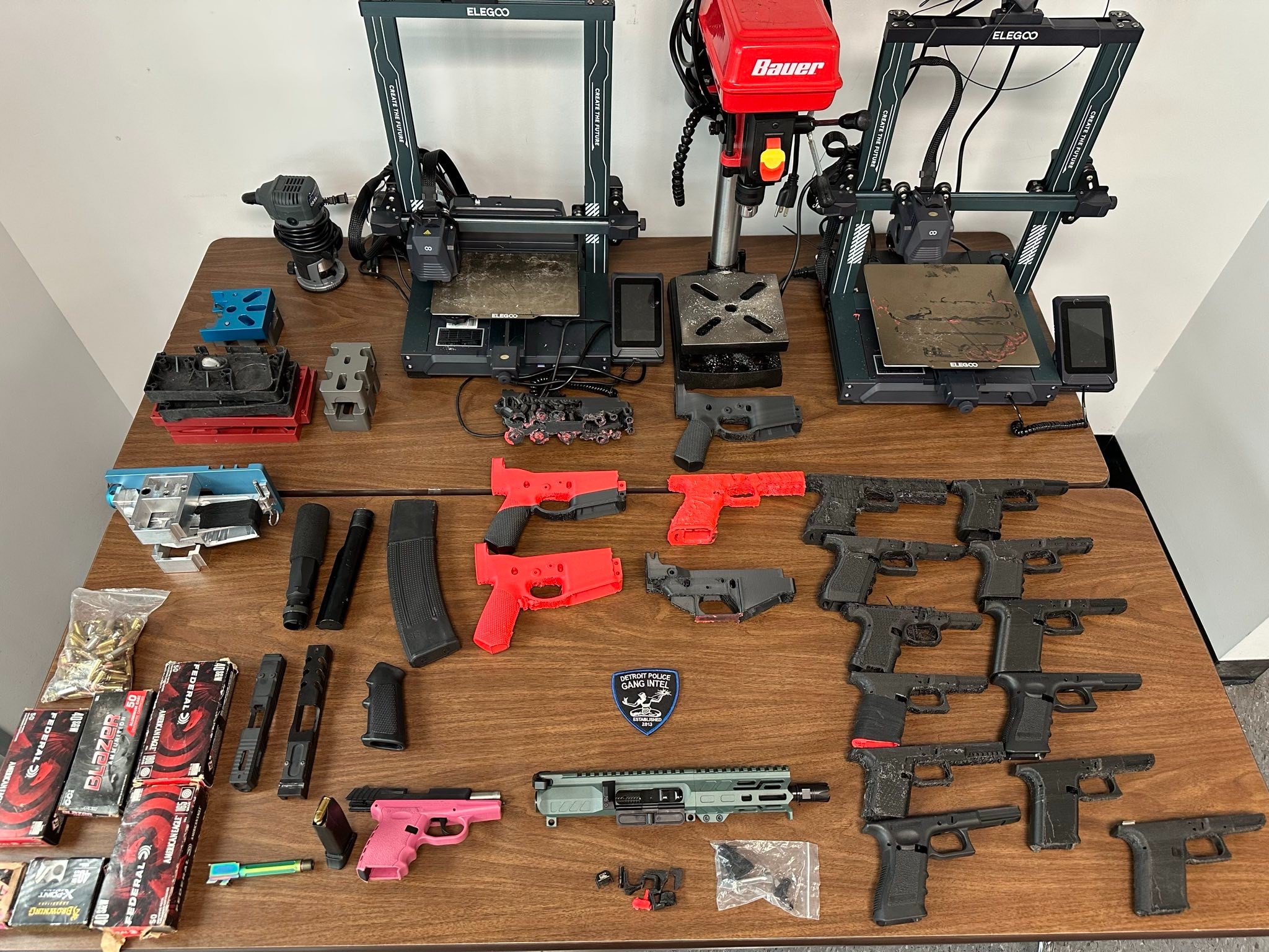 A flat-lay on wooden table of a collection of 3D-printed firearms and equipment seized from a 14-year-old's manufacturing operation in his home.